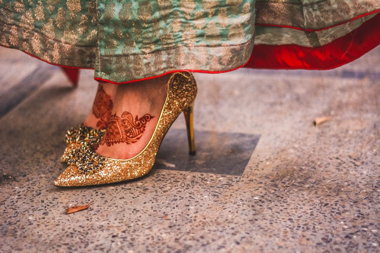 Close-up of gold high heels and henna design on a woman's feet at a festive event.